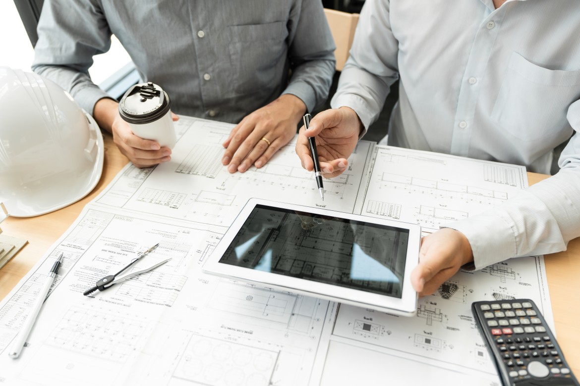 Team of construction professionals reviewing digital blueprints and cost data on a tablet